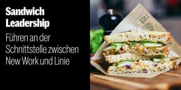 Aufgeschnittenes belegtes Sandwich in Butterbrotpapier auf einem Holzbrett, dahinter Salat und eine Flasche