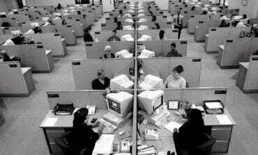 Großraumbüro der Taylor-Ära in Schwarz-Weiß: Dutzende identische Cubicles in strengen Reihen, jeweils mit Röhrenmonitor und Aktenstapel